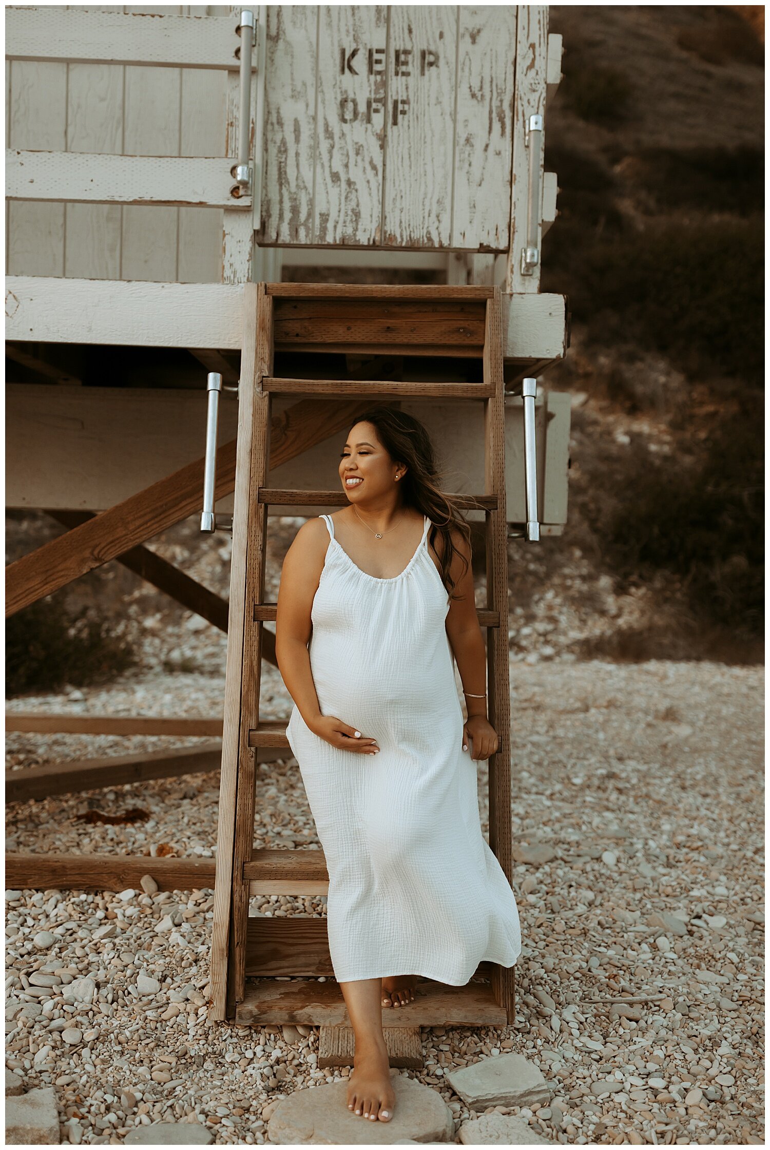 mama holding her belly while looking out on the ocean during her maternity session on Los Angeles beach